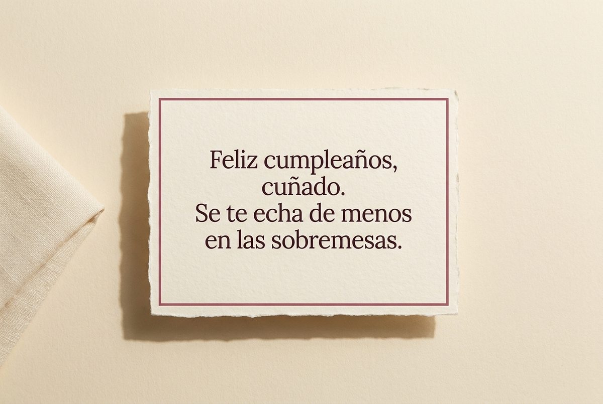 Tarjeta de cumpleaños de papel crema hecho a mano, con borde deckle y un filete impreso en rosa oscuro, fotografiada en plano cenital. En la tarjeta se lee «Feliz cumpleaños, cuñado. Se te echa de menos en las sobremesas.». Al lado, una servilleta de lino crema doblada en el borde izquierdo.