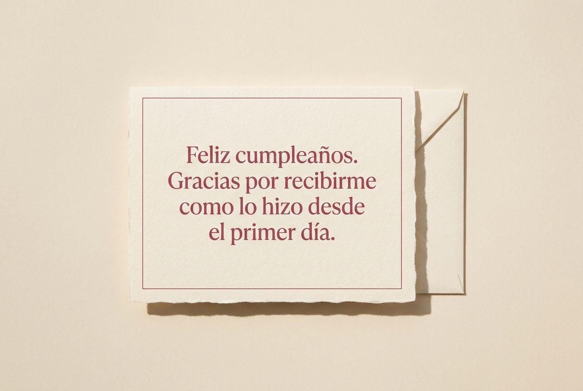 Tarjeta de cumpleaños de papel crema hecho a mano, con borde deckle y un filete impreso en rosa oscuro, fotografiada en plano cenital. En la tarjeta se lee «Feliz cumpleaños. Gracias por recibirme como lo hizo desde el primer día.». Al lado, un sobre crema cuadrado detrás, por el lado derecho.
